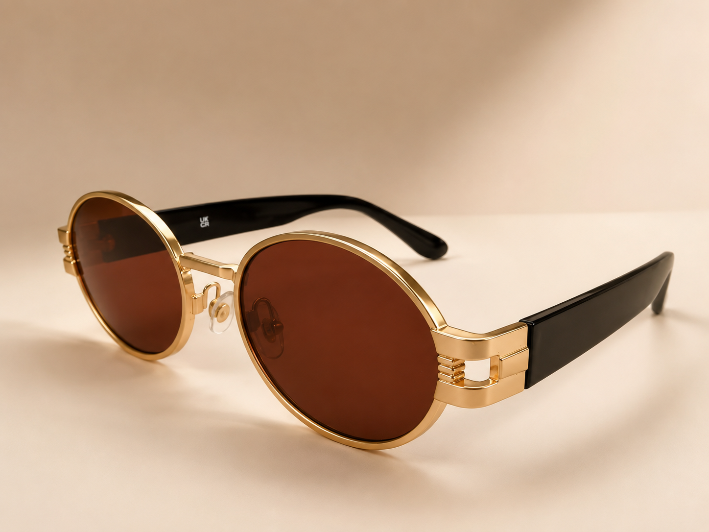 Front view of gold oval sunglasses with warm brown lenses and black side arms
